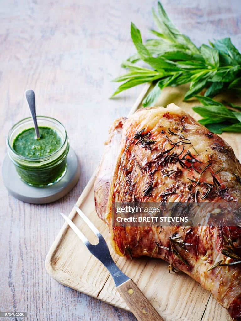 Roast leg of lamb on chopping board with jar of mint sauce, close-up