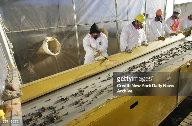 Recovery workers in protective gear examine debris from the World Trade Center as it travels along a conveyor belt in a plastic-covered "hothouse"...