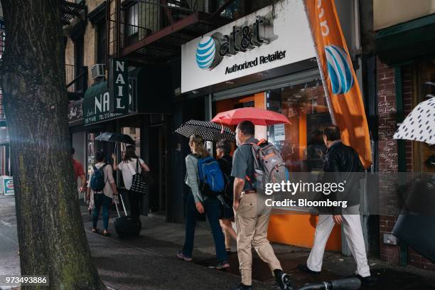 Pedestrians carry umbrellas while passing in front of an AT&T Inc. Store location in New York, U.S., on Wednesday, June 13, 2018. AT&T Inc.'s...