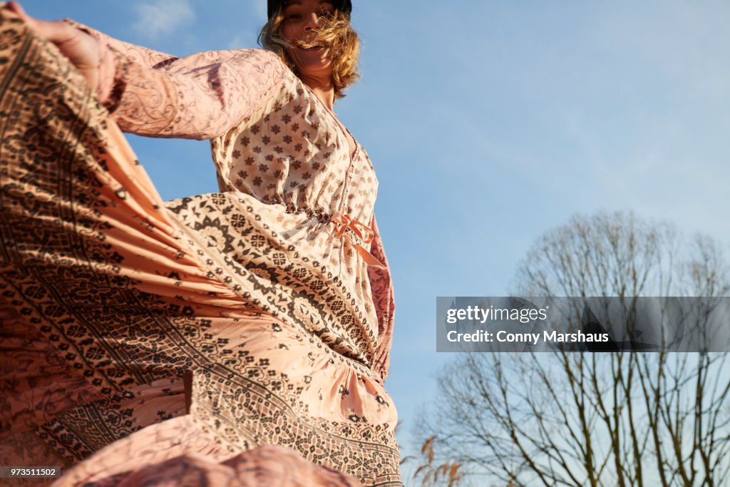 Hippy style woman dancing against blue sky, low angle view