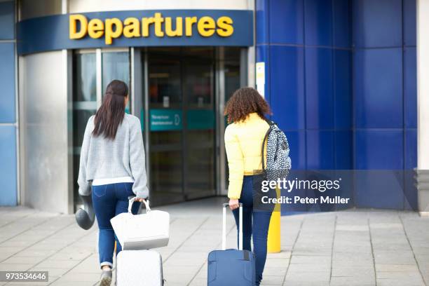 women pulling wheeled suitcases to airport terminal, rear view - airport uk stock-fotos und bilder