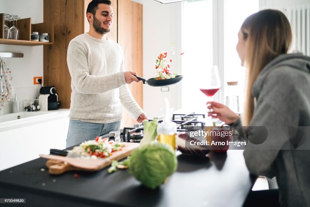 Couple cooking food, tossing vegetables in frying pan
