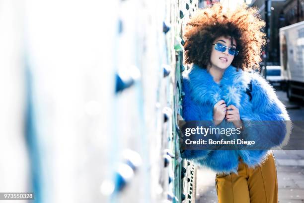 portrait of woman with afro hair wearing fur coat, leaning against wall looking at camera - funky woman stock pictures, royalty-free photos & images