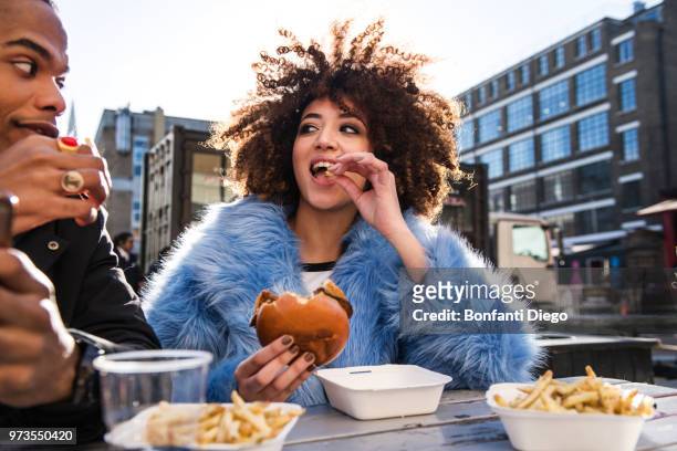 young couple eating burger and chips outdoors - unhealthy eating ストックフォトと画像
