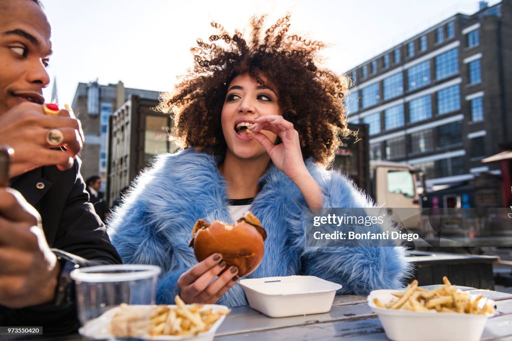 Young couple eating burger and chips outdoors