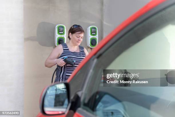 woman charging electric car at city charging point - monty shadow stockfoto's en -beelden