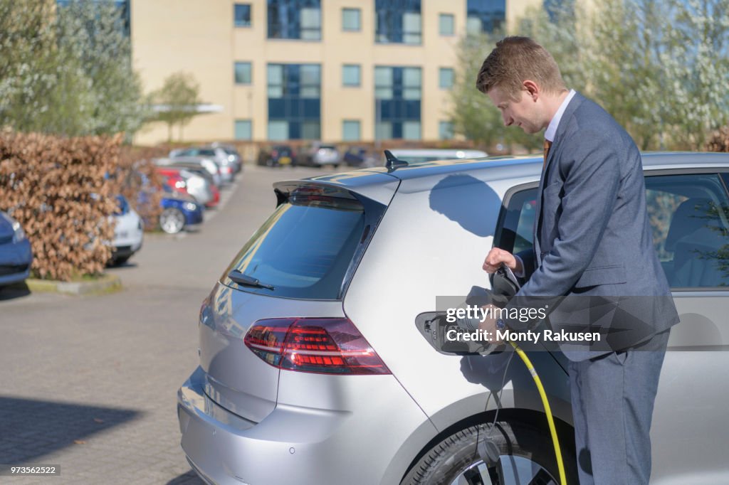 Businessman charging electric car at charging point in business park