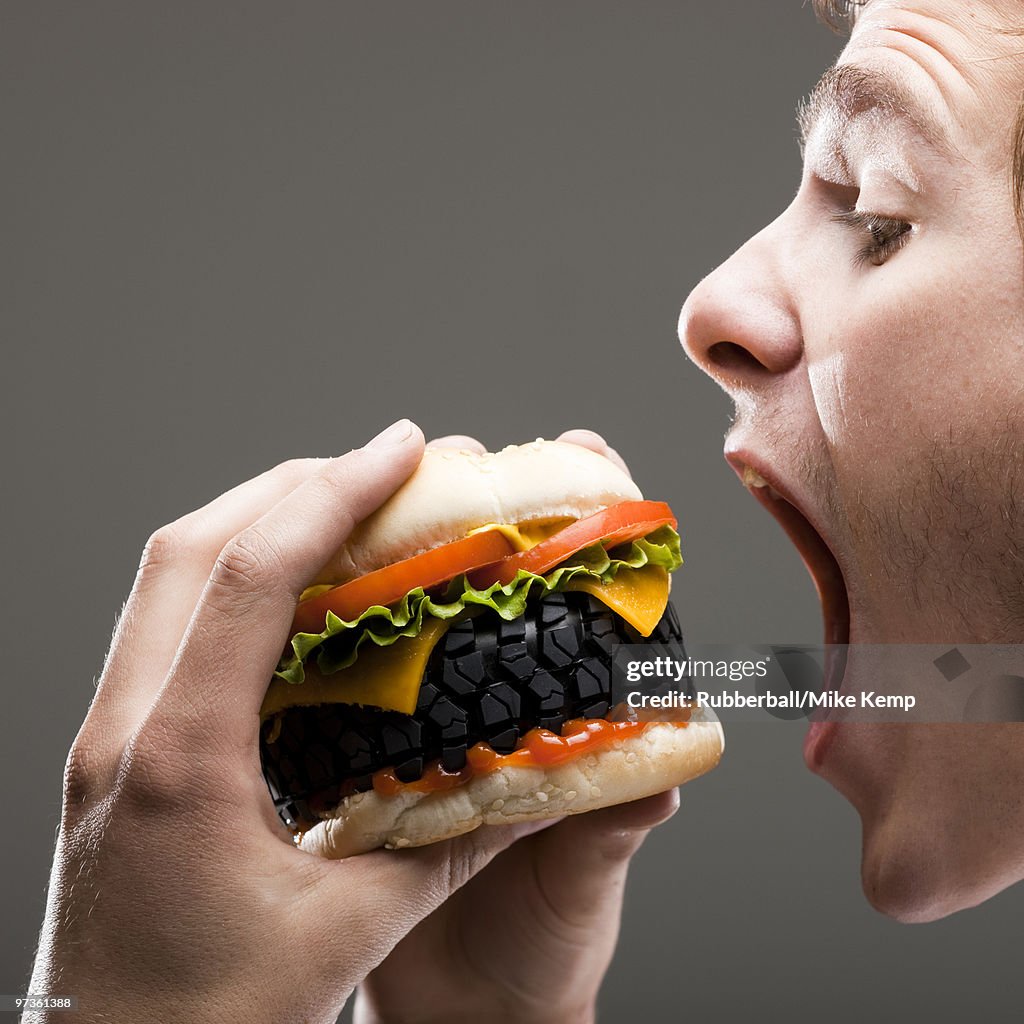 Side view of young man about to bite a tire hamburger, close up