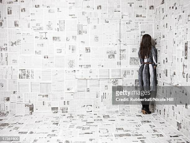 rear view of young woman standing in corner of newspapers covered room, studio shot - paper corner stock pictures, royalty-free photos & images