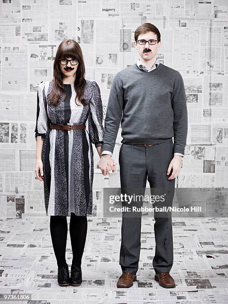 two young people with fake mustache standing in newspapers covered room, studio shot - groucho marx disguise stock pictures, royalty-free photos & images