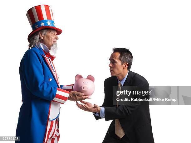 man in uncle sam's costume giving piggybank to other man, studio shot - boomer banks fotografías e imágenes de stock