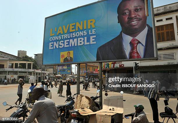 Man sits on March 2, 2010 in Lome under a billboard of Togo�s incumbent President Faure Gnassingbe, who came to power in 2005 after the death of his...