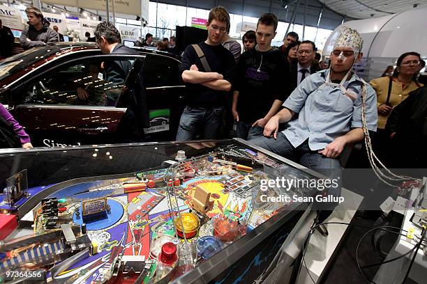 Man, wearing an EEG brain scanning apparatus on his head, plays a pinball game solely through willing the paddles to react with his brain at the...