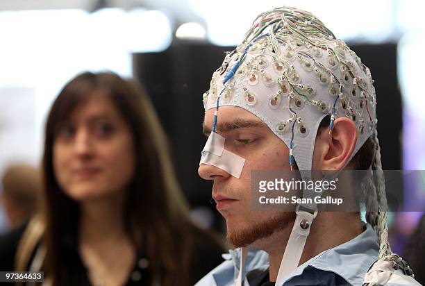 Young woman watches a man, wearing an EEG brain scanning apparatus on his head, play a pinball game solely through willing the paddles to react with...