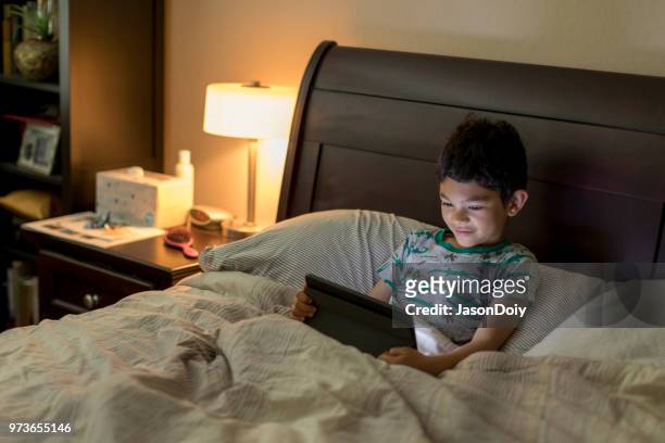 garçon avec tablette dans le lit - jasondoiy photos et images de collection