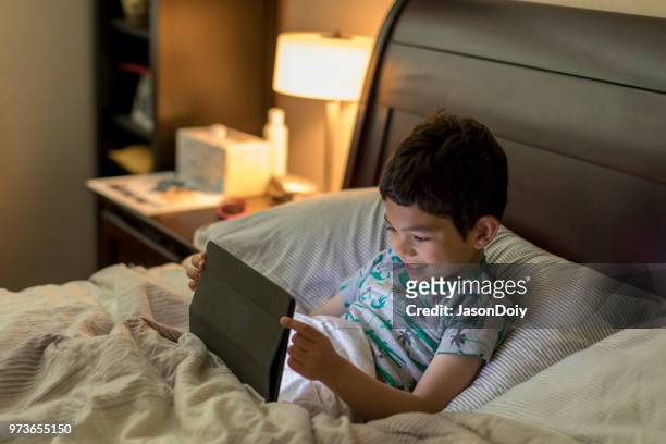 boy with tablet computer in bed - jasondoiy stock pictures, royalty-free photos & images