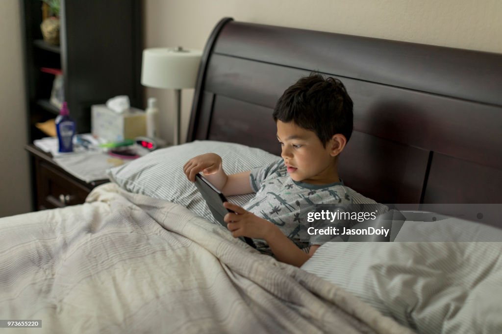 Junge mit Tablet-PC im Bett