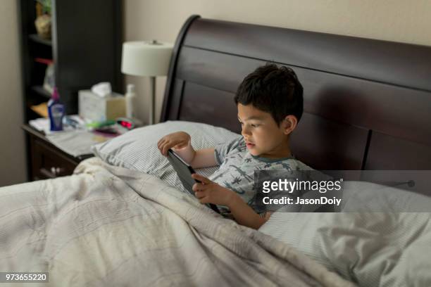 garçon avec tablette dans le lit - jasondoiy photos et images de collection