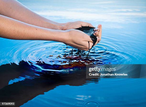 pollution running through hands into water - oil slick stock pictures, royalty-free photos & images