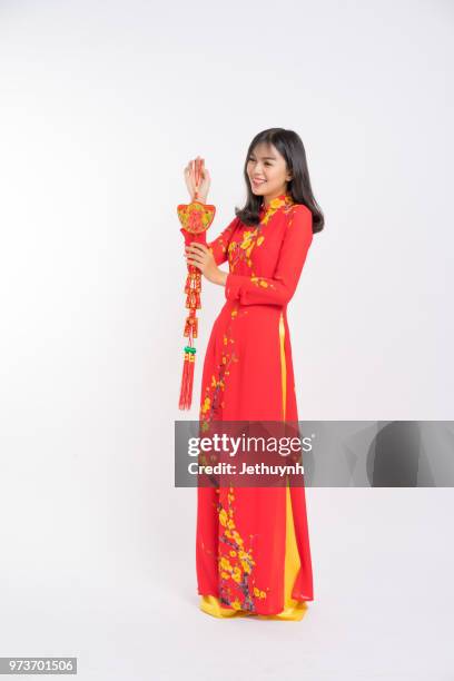 young woman wearing vietnamese red color ao dai, smiling, holding a lucky firecracker for new year to wish lucky and rich. - jethuynh stock pictures, royalty-free photos & images