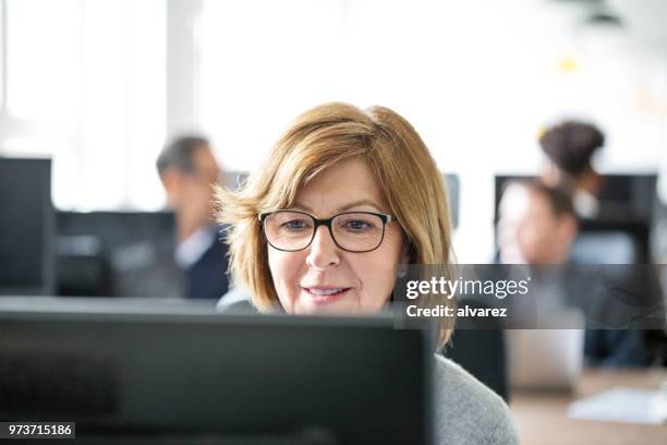 reife geschäftsfrau arbeiten an ihrem schreibtisch im büro - büro arbeiten hintergrund unscharf stock-fotos und bilder