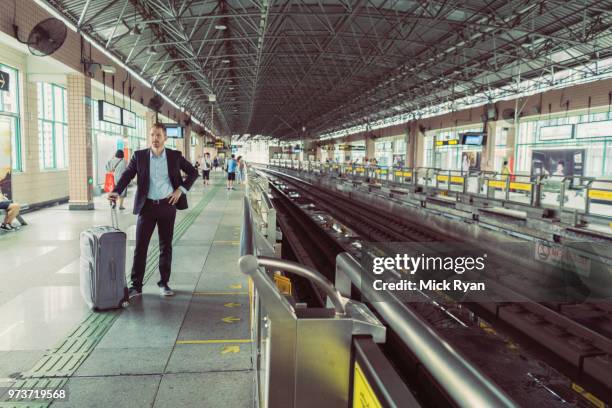 businessman with wheeled suitcase, standing at train station, waiting for train - asian waiting angry expressions stock pictures, royalty-free photos & images