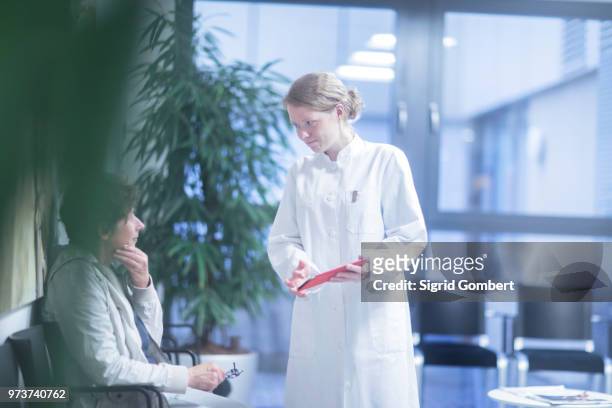 radiologist, holding digital tablet, talking to mature woman in waiting area of hospital - sigrid gombert stock-fotos und bilder