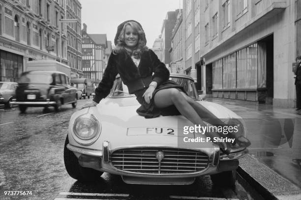British fashion model and actress Fiona Richmond pictured while sitting on the hood of a car, London, UK, 11th January 1974.