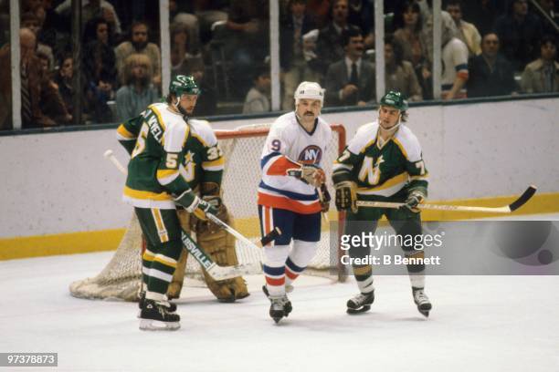 Bryan Trottier of the New York Islanders skates past the low slot area between Brad Maxwell and Neal Broten of the Minnesota North Stars during the...