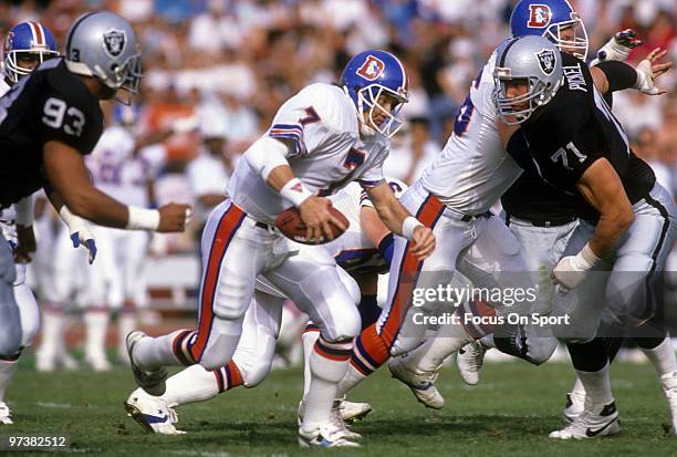 S: Quarterback John Elway of the Denver Broncos scrambles away from defensive linemen Bill Pickel and Greg Townsend of the Los Angeles Raiders circa...