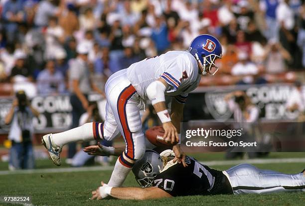 S: Quarterback John Elway of the Denver Broncos get away from the grasp of defensive tackle Scott Davis of the Los Angeles Raiders circa 1980's...