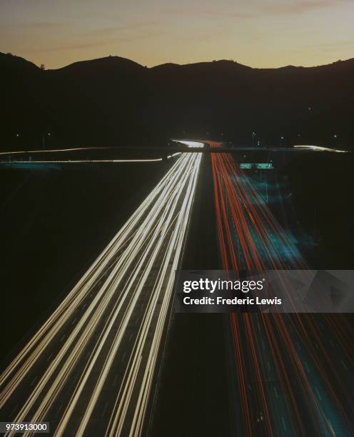 Light trails from vehicles on a highway at dusk, near exits for Moraga Drive and Mulholland Drive, Los Angeles, California, circa 1970.