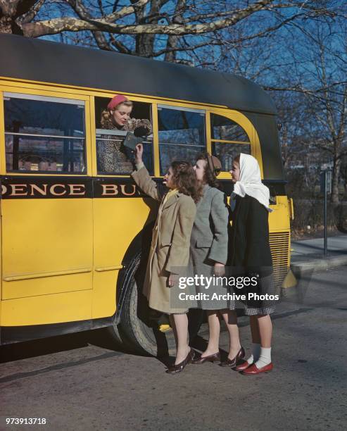 Teenage girl passes her autograph book to a young woman bus passenger, circa 1950.