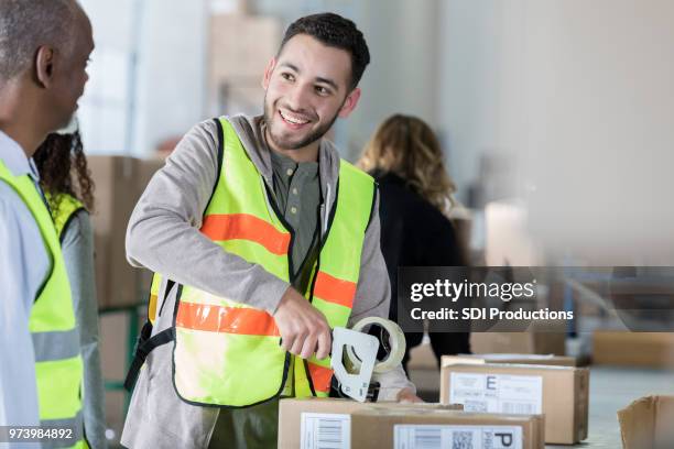 male distribution warehouse employee seals package - tape dispenser stock pictures, royalty-free photos & images
