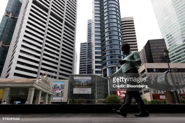 Man using a mobile phone walks past commercial buildings in the central business district of Singapore, on Wednesday, June 13, 2018. Tourism as well...