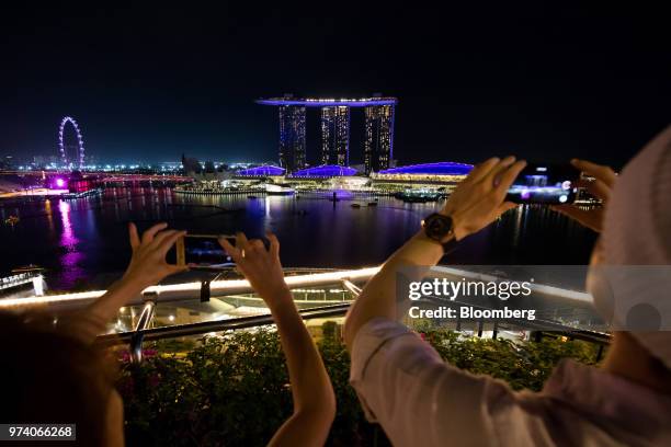 People take photographs of the Marina Bay Sands hotel and casino, center, and Singapore flyer illuminated at night in Singapore, on Wednesday, June...