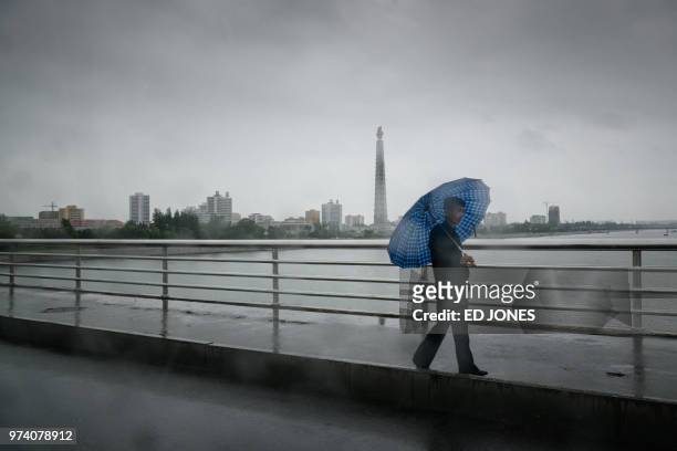 Pedestrian shelters beneath an umbrella as he walks across a bridge over the Taedong river before the landmark Juche tower, during rainfall in...