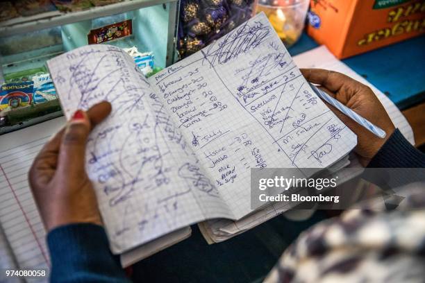 Janeffer Wacheke, co-owner of a fresh-vegetable stall, checks her account notebook at her stall in Nairobi, Kenya, on June 11, 2018. Wacheke's...