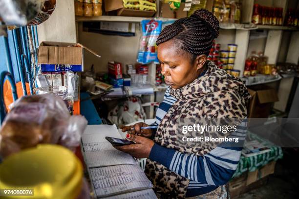 Janeffer Wacheke, co-owner of a fresh-vegetable stall, checks her mobile phone for a purchase order of vegetables and fruits made to Twiga Foods...