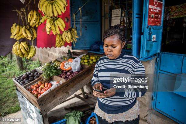 Janeffer Wacheke, co-owner of a fresh-vegetable stall, checks her mobile phone for a purchase order of vegetables and fruits made to Twiga Foods...