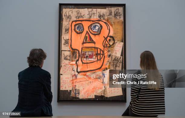 Man and woman sit on a bench in front of 'Untitled' by Jean-Michel Basquiat during a preview of the Contemporary Art sale at Sotheby's on June 14,...