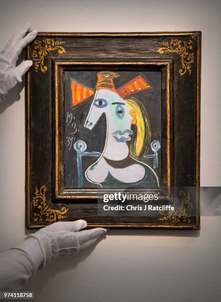 An art handler adjusts 'Tete de femme au chapeau orange' by Pablo Picasso during a preview of the Impressionist and Modern sale at Sotheby's on June...