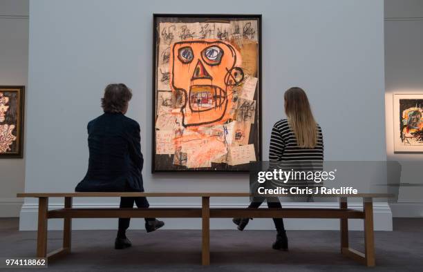 Man and woman sit on a bench in front of 'Untitled' by Jean-Michel Basquiat during a preview of the Contemporary Art sale at Sotheby's on June 14,...