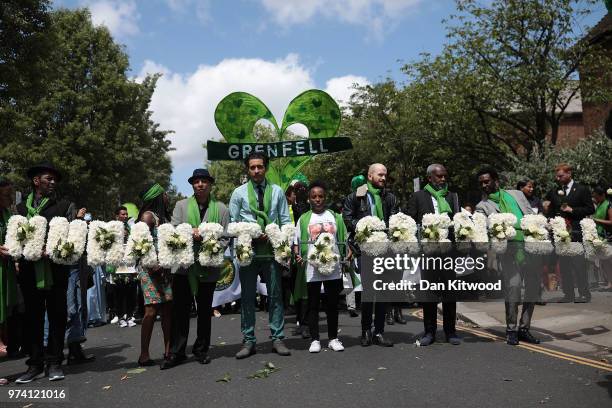 People hold tributes made of white roses which spell out 'Humanity' and 'Grenfell' as they walk to the Wall of Truth to mark the one year anniversary...