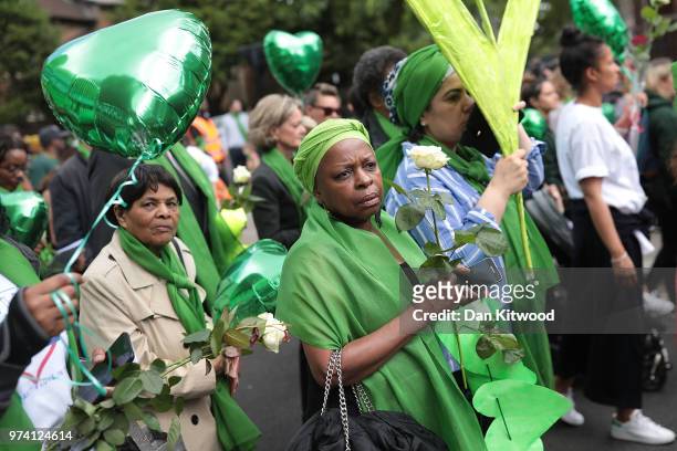People hold up green balloons and white roses as they walk to the Wall of Truth to mark the one year anniversary of the Grenfell Tower fire on June...