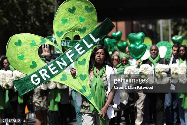 People hold tributes as they walk to the Wall of Truth to mark the one year anniversary of the Grenfell Tower fire on June 14, 2018 in London,...