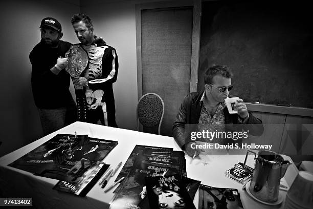 Fan poses with David Arquette, wearing a skeleton costume and holding his World Wrestling Championship belt, while actor Thomas Jane signs autographs...