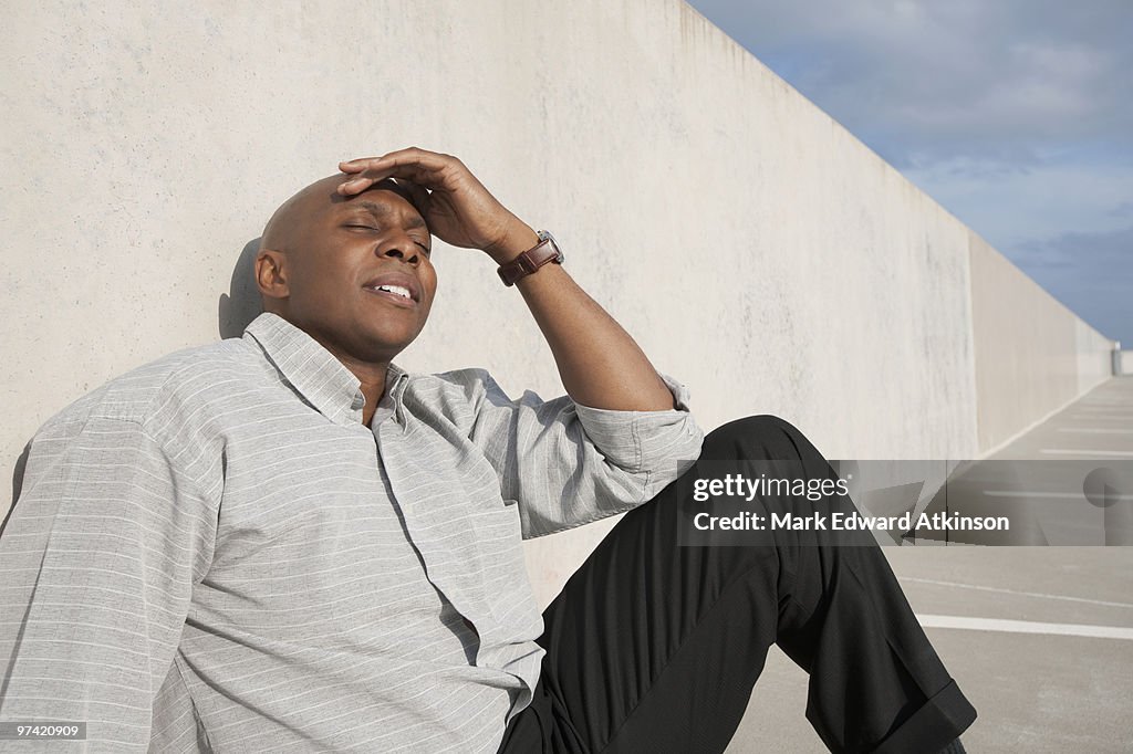 African businessman sitting on ground in parking lot