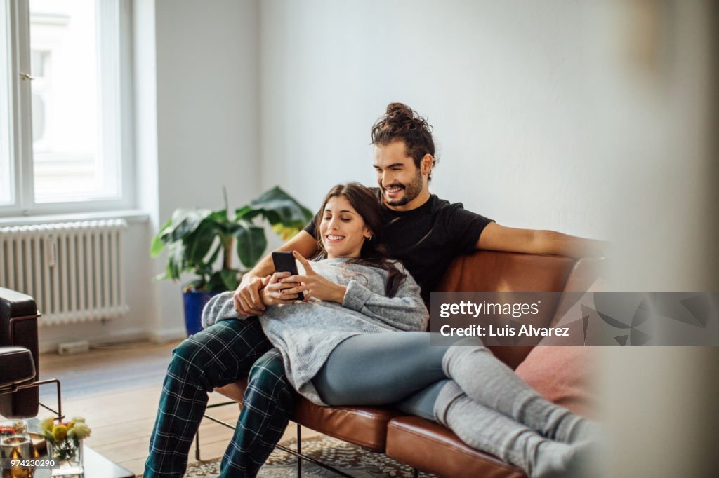 Young couple with mobile phone relaxing on sofa