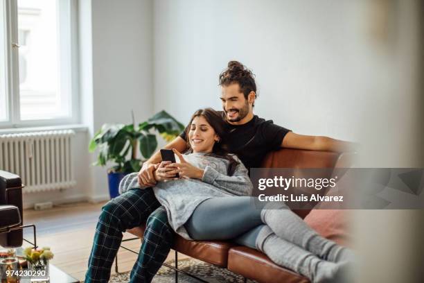 young couple with mobile phone relaxing on sofa - jong koppel stockfoto's en -beelden
